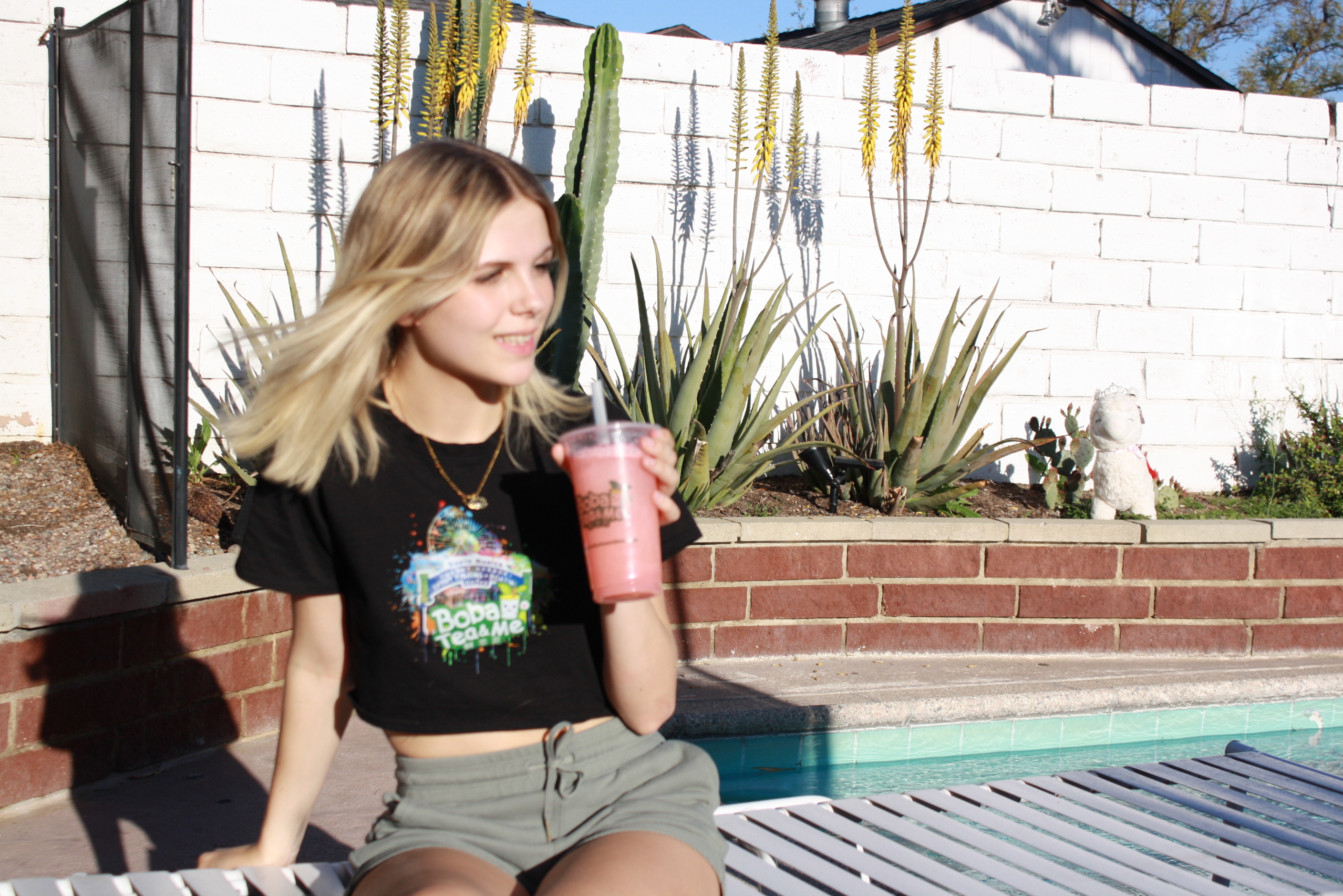 A student holding a pink Boba Tea & Me drink outside by the pool.